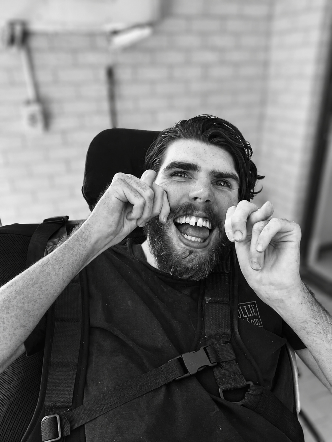 Eamon, a young man in a wheelchair with a supportive chest harness, laughing.
