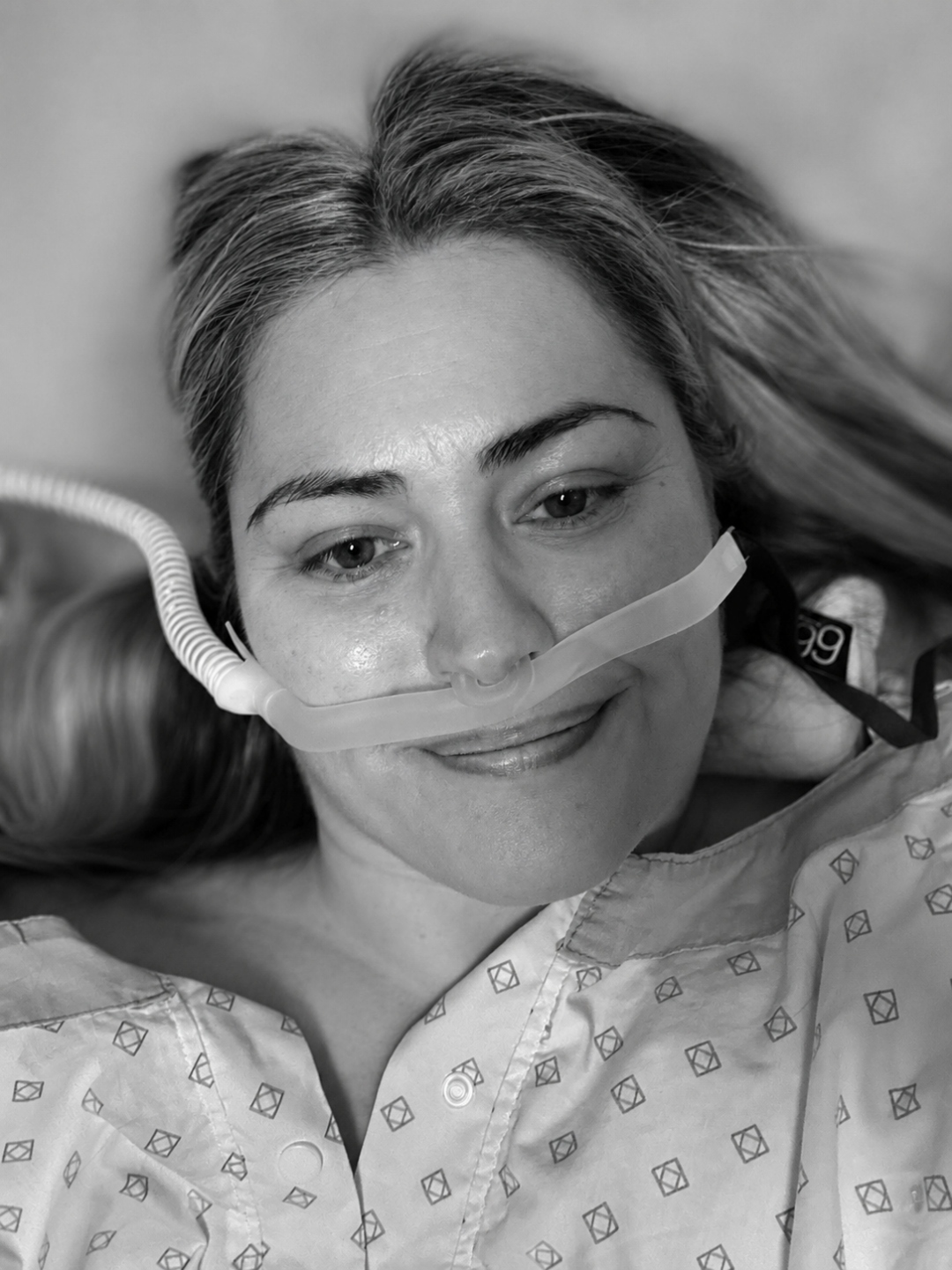 Marayke Jonkers lying in a hospital bed, wearing a hospital gown and a nasal cannula.