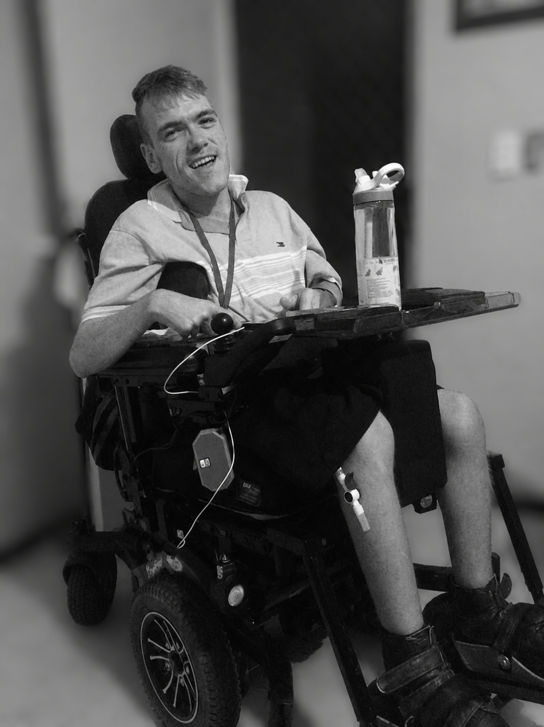 Peter Hall, a man in a power wheelchair with a water bottle on his tray, smiling.
